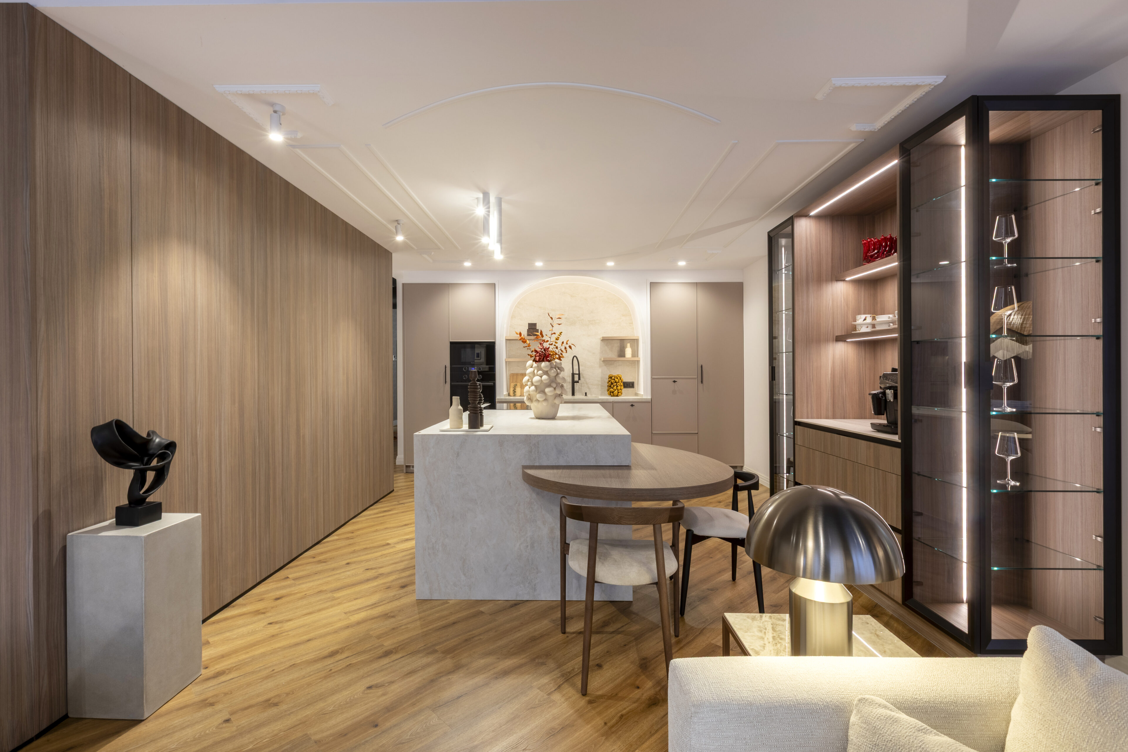 Cocina de diseño premium con isla de cuarzo, muebles en madera y vitrina iluminada; ambiente moderno. NEXO Küchen Cocina moderna con isla central, muebles en madera clara y vitrina iluminada